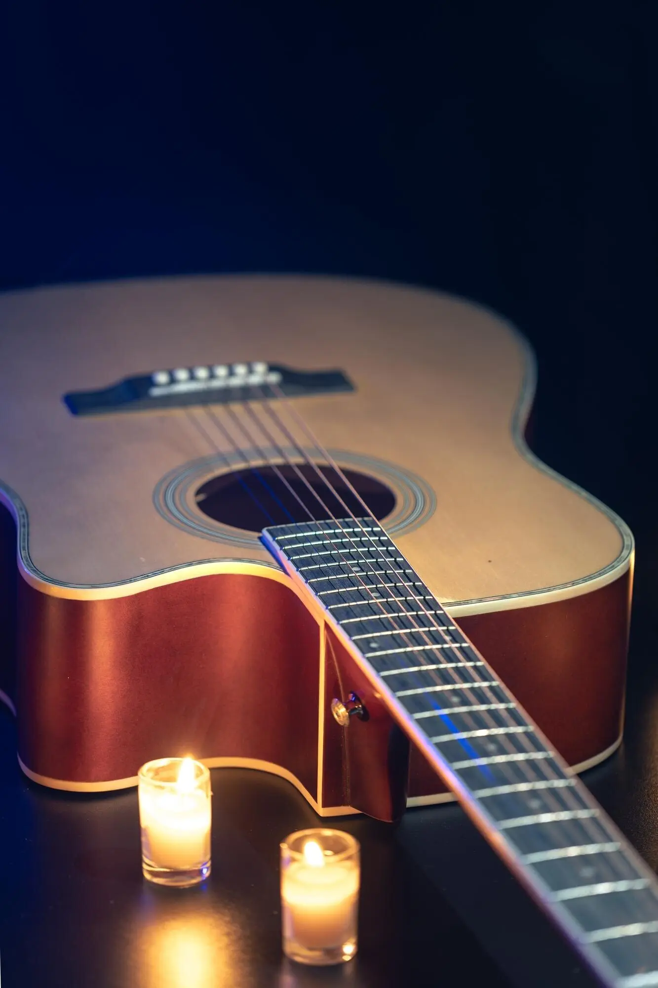 Akustische Gitarre vor schwarzem Hintergrund mit Kerzen