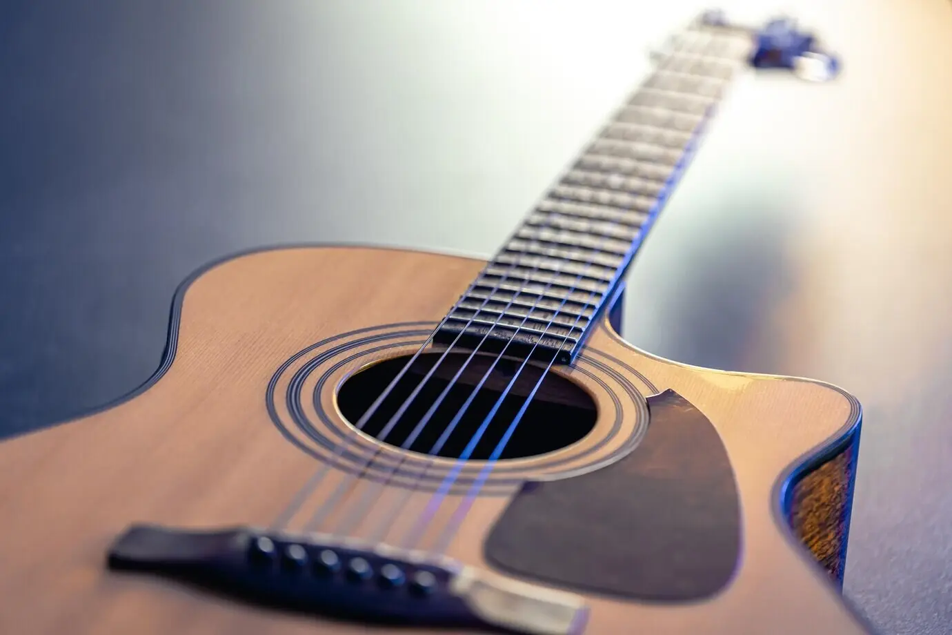 Eine akustische Gitarre als Musikinstrument ruht vor einem dunkelschwarzen Hintergrund.